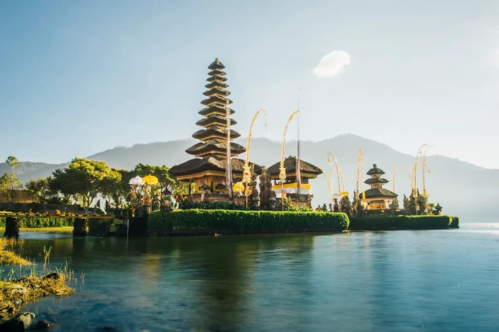 Pura di tepi danau dengan meru bertingkat dan pegunungan berkabut di belakangnya