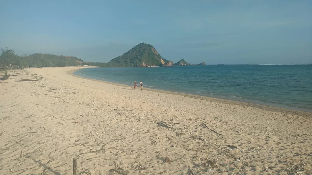 Pantai pasir putih yang panjang dan sepi dengan bukit hijau di ujung teluk